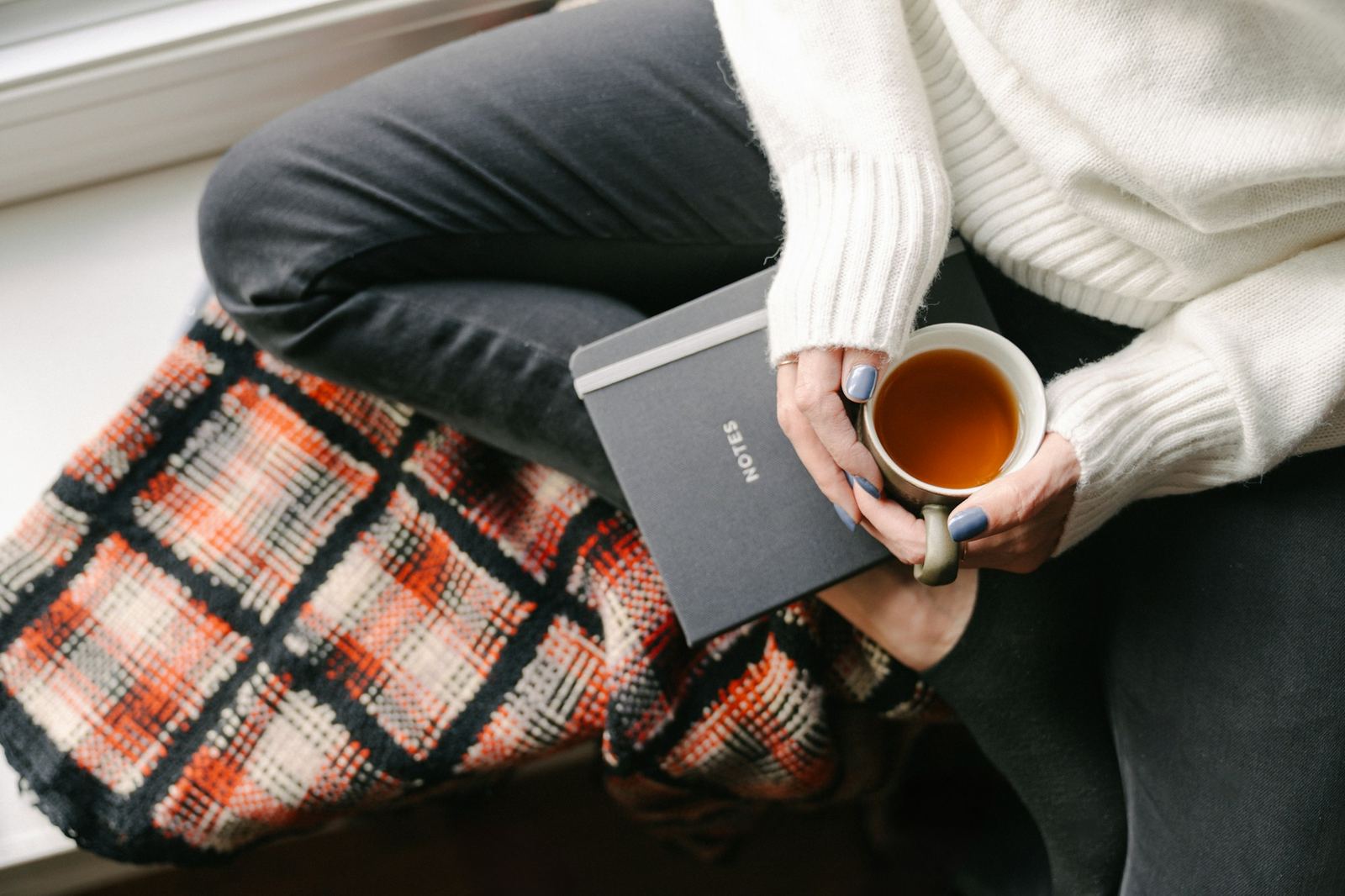 Someone sitting on a windowsill with a mug of tea and a blanket